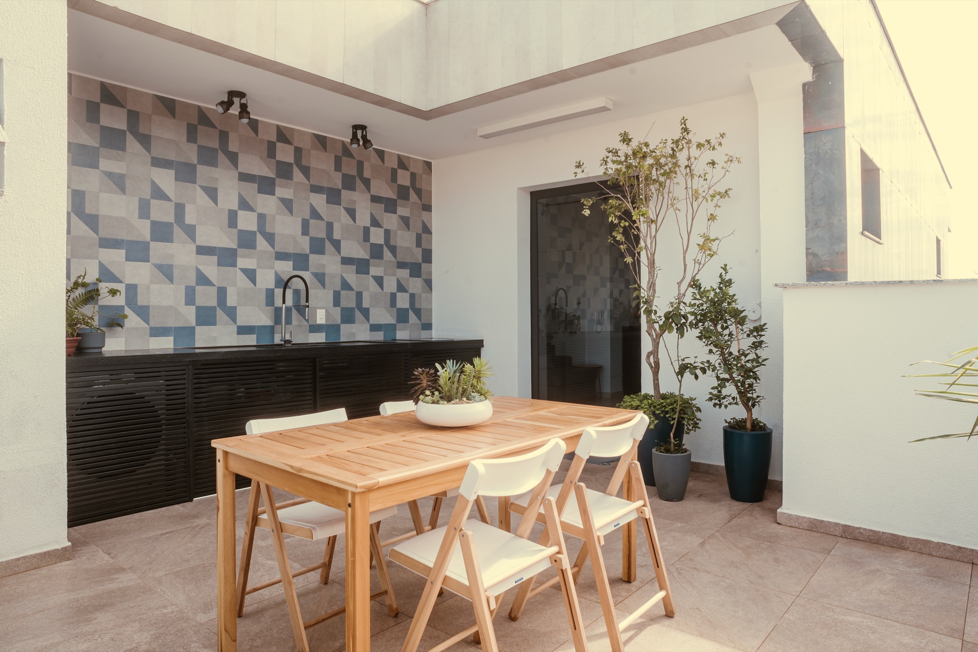 Área externa com mesa de madeira e revestimento geométrico, projeto do Estúdio Leme